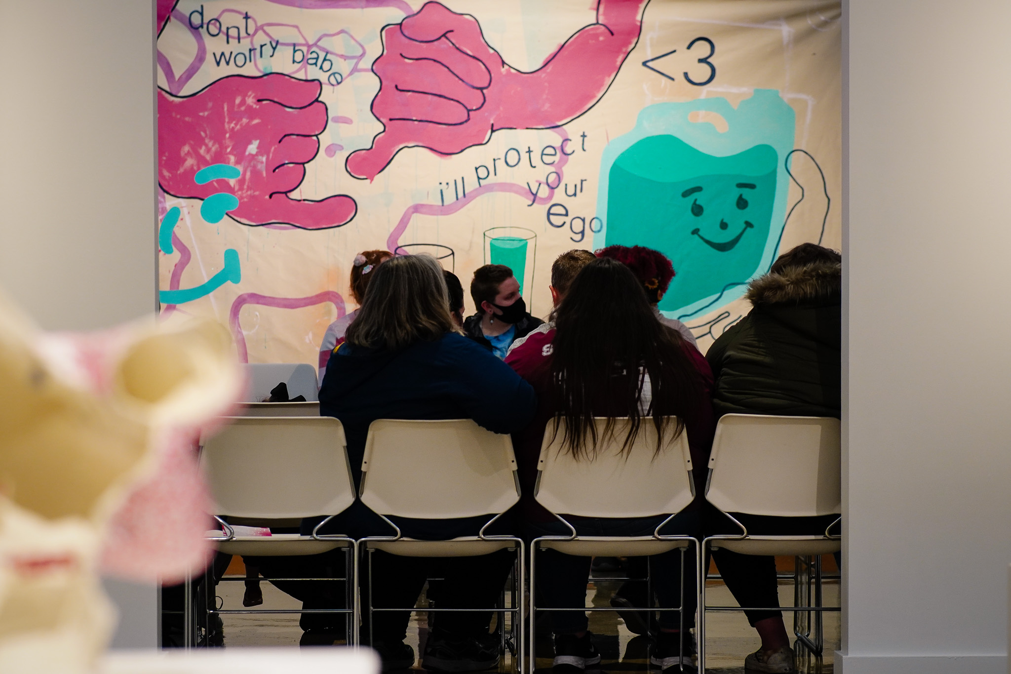 A small group of people sits in front of large, unstretched canvas painting from the 2022 Master of Arts in Studio exhibition.